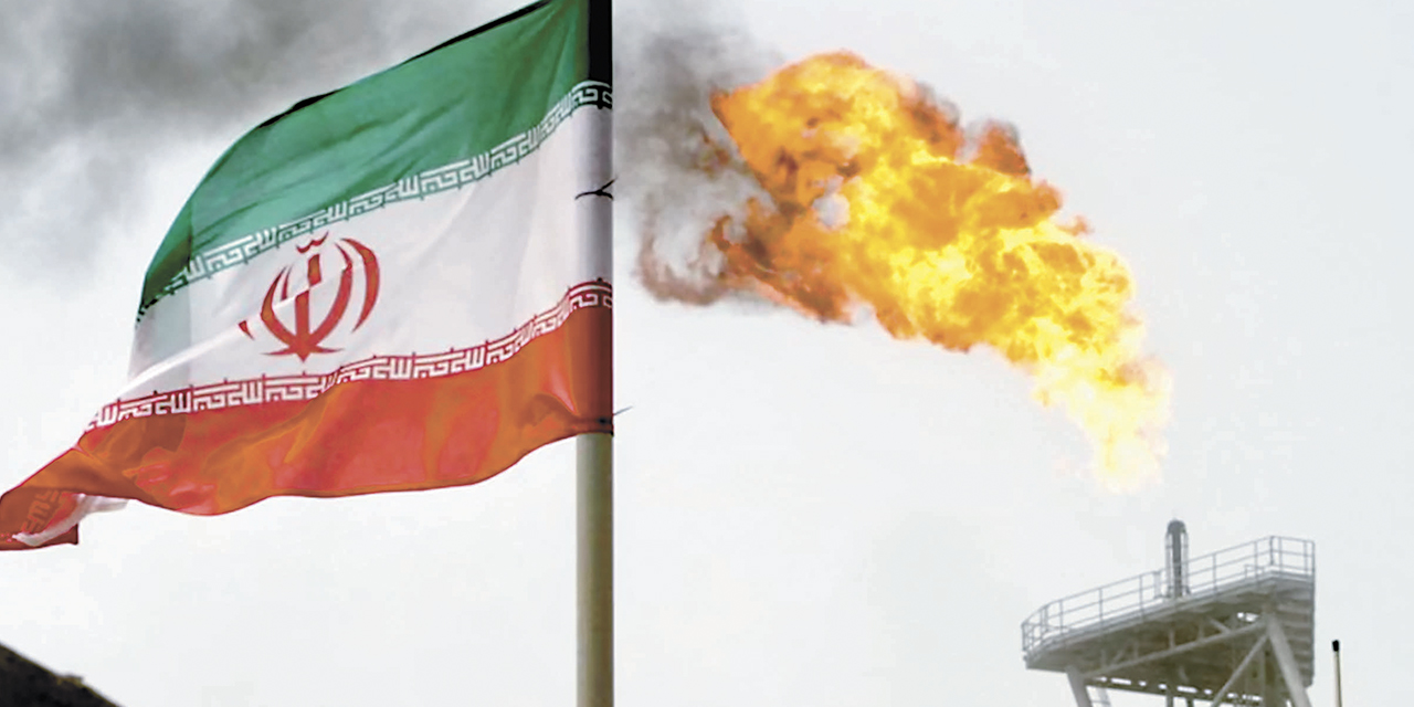Una antorcha de gas en una plataforma de producción de petróleo junto a una bandera iraní en el Golfo.