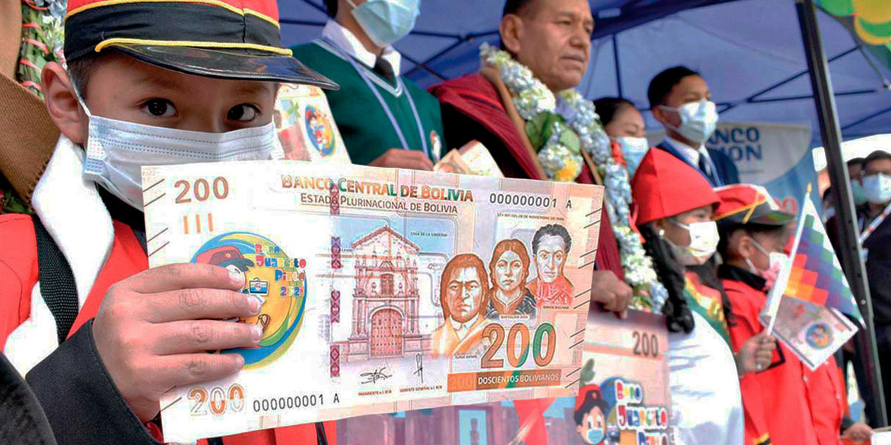Un niño muestra un billete simbólico que representa al Bono Juancito Pinto, una conquista social.